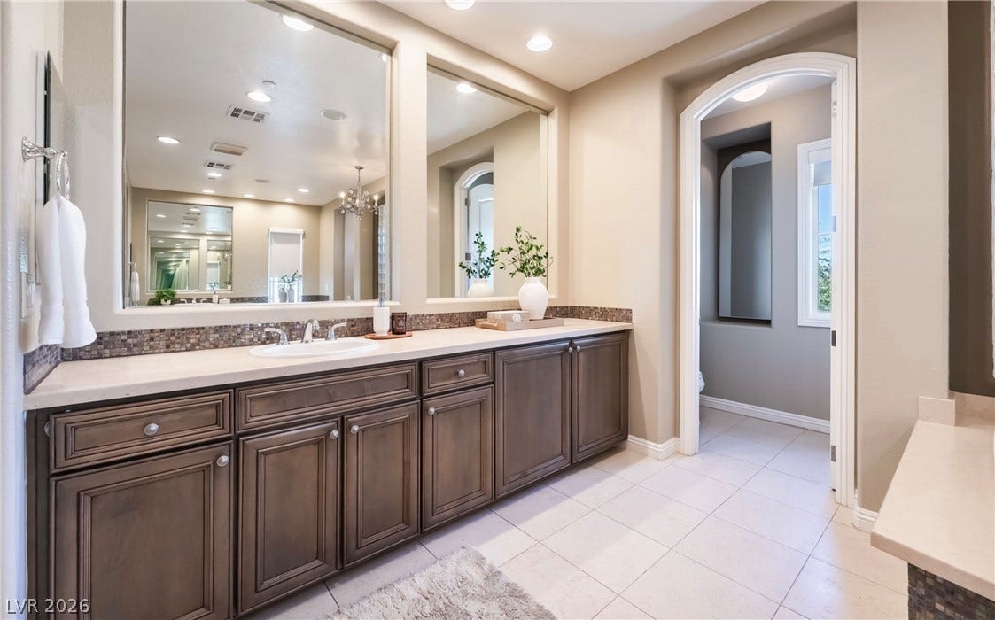 1343 Quiet River Avenue, Henderson, NV 89012 An arched doorway opens to a tile floor bathroom featuring custom wood vanities.