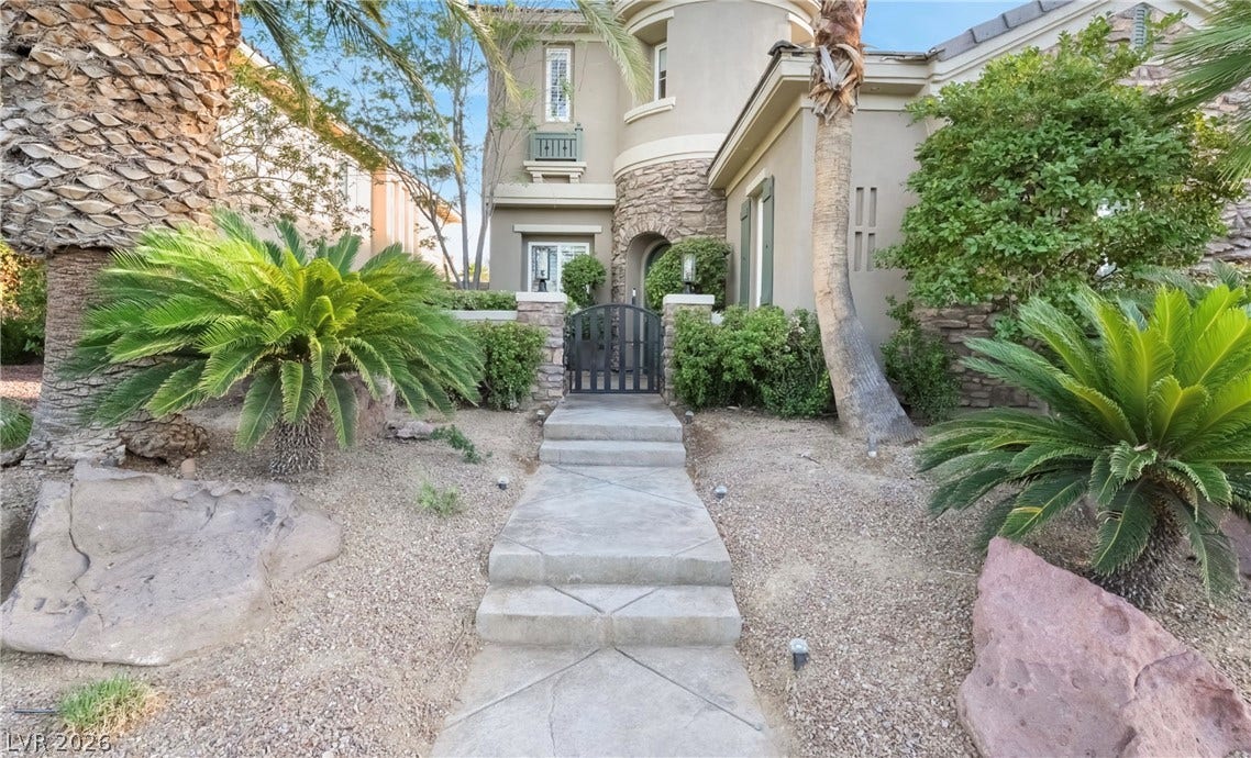 1343 Quiet River Avenue, Henderson, NV 89012 Concrete steps lead toward a gated stone entry surrounded by desert landscaping and palm trees.