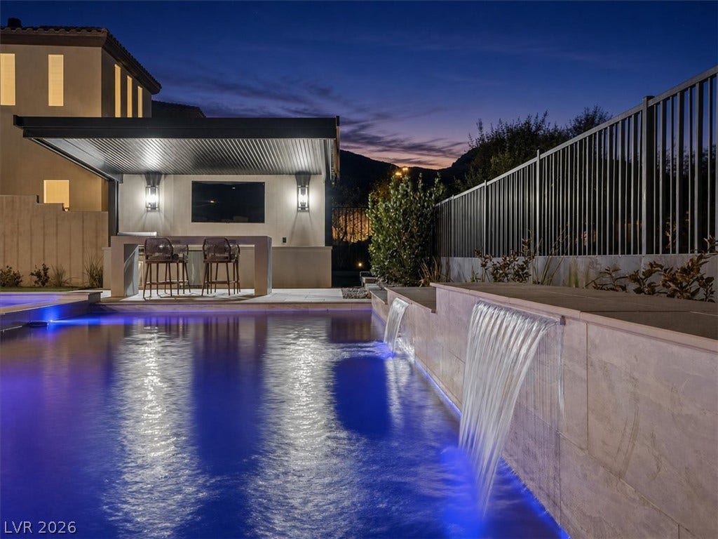 Dramatic waterfalls cascade into a glowing swimming pool beneath a covered outdoor bar area.