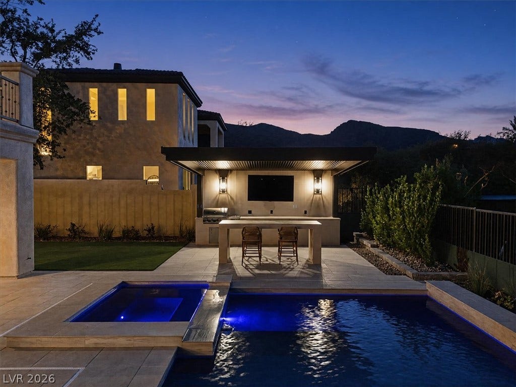 A stone patio area with a swimming pool and covered outdoor kitchen faces mountain views.