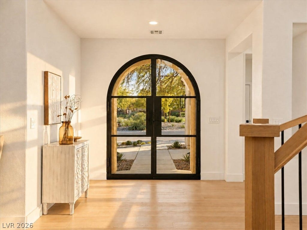 An arched glass entryway opens to light-filled interiors with light wood flooring.