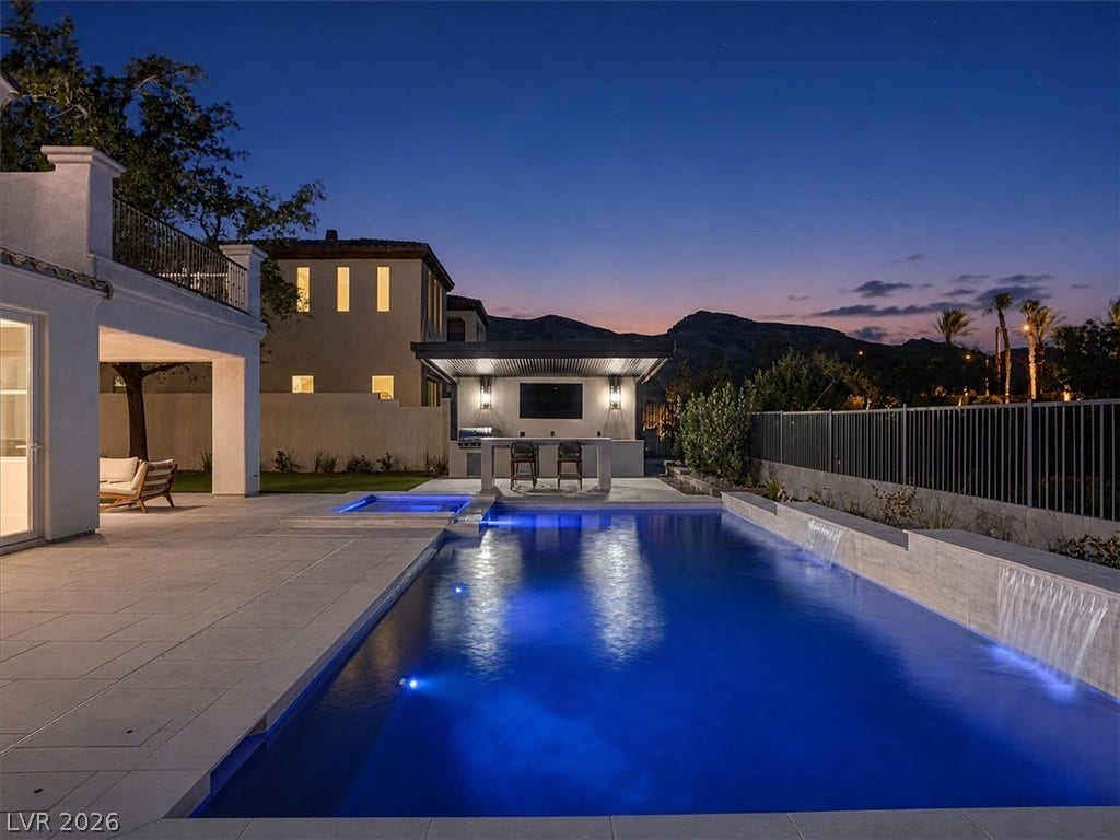 An inviting swimming pool and custom outdoor kitchen glow against a twilight mountain backdrop.
