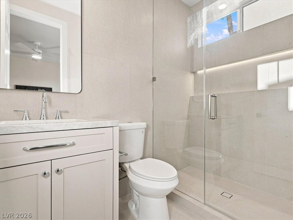 A glass-enclosed walk-in shower features neutral tile and a modern vanity.