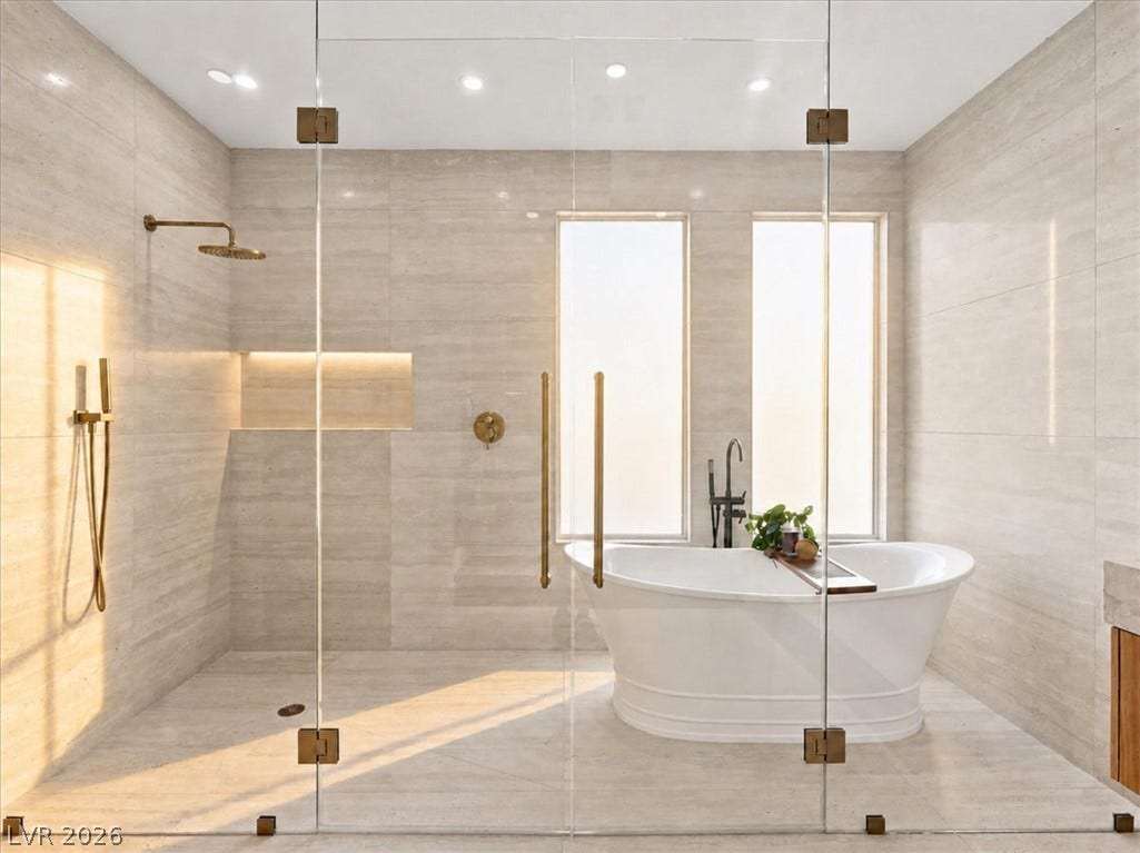 Gleaming stone tile walls surround a freestanding soaking tub and glass-enclosed walk-in shower.