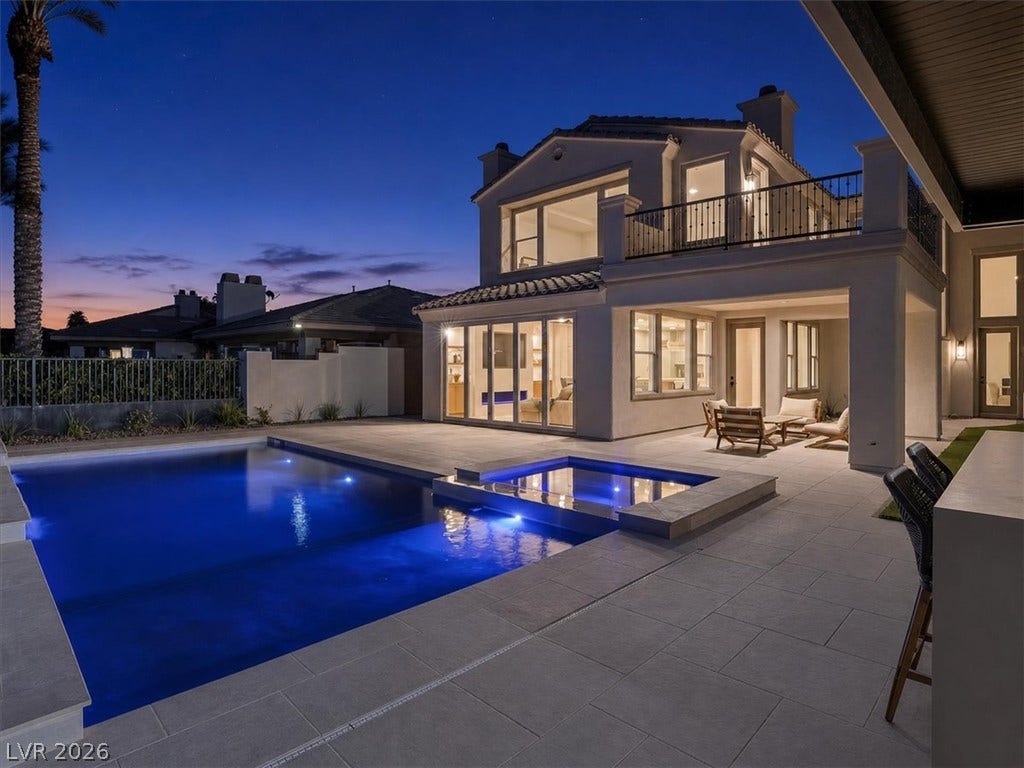 An inviting backyard oasis centers around a pristine swimming pool and spa beneath twilight skies.