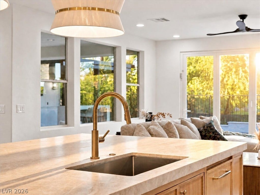 A spacious stone-topped kitchen island overlooks the sunlit open-concept living area and backyard beyond.
