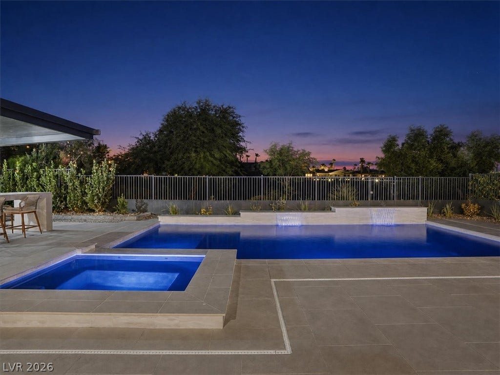 A pristine swimming pool and spa are surrounded by elegant stone tiling under evening skies.
