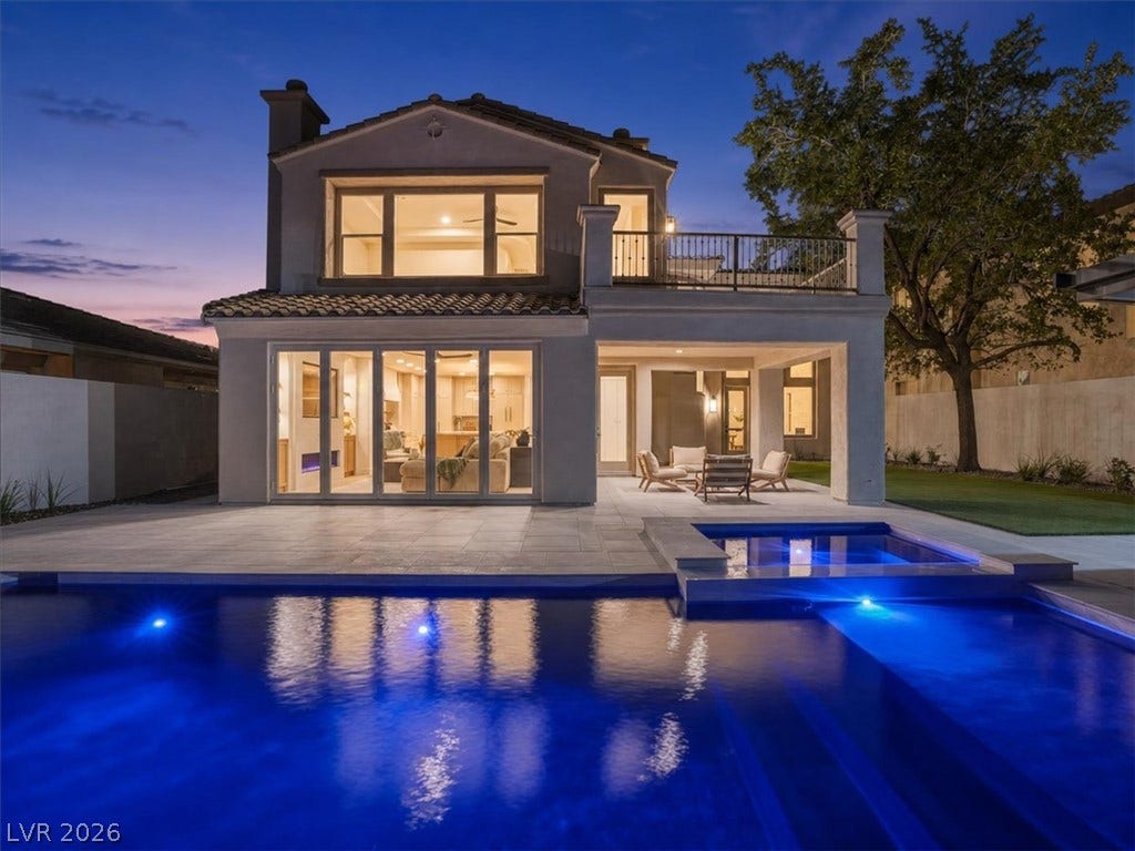 A sparkling pool and stone terrace extend from the elegant two-story stucco exterior.