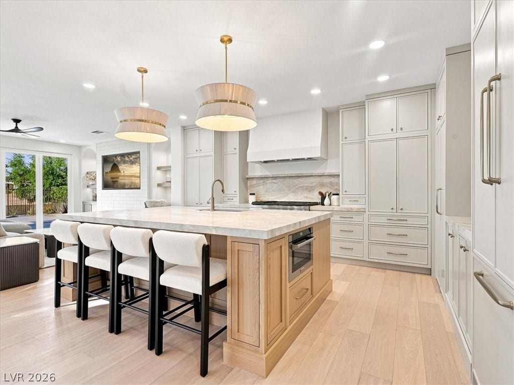 An oversized central island anchor this light-filled culinary space featuring custom cabinetry and hardwood flooring.
