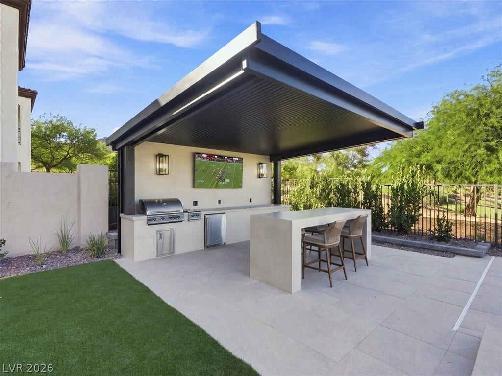 A modern covered pavilion houses a premium outdoor kitchen with stone counters and a bar island.