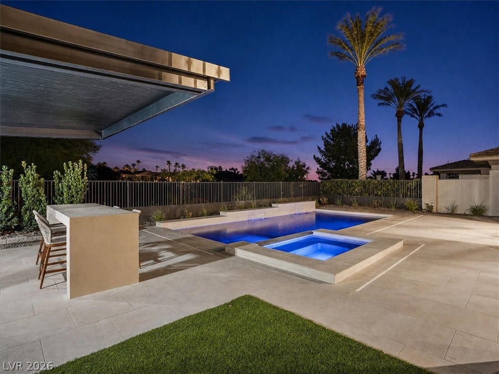An inviting backyard oasis features a shimmering pool and spa beneath towering palm trees.