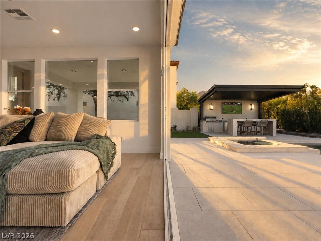 Seamless transition leads from the hardwood-floored interior to a spacious paved patio with outdoor kitchen.