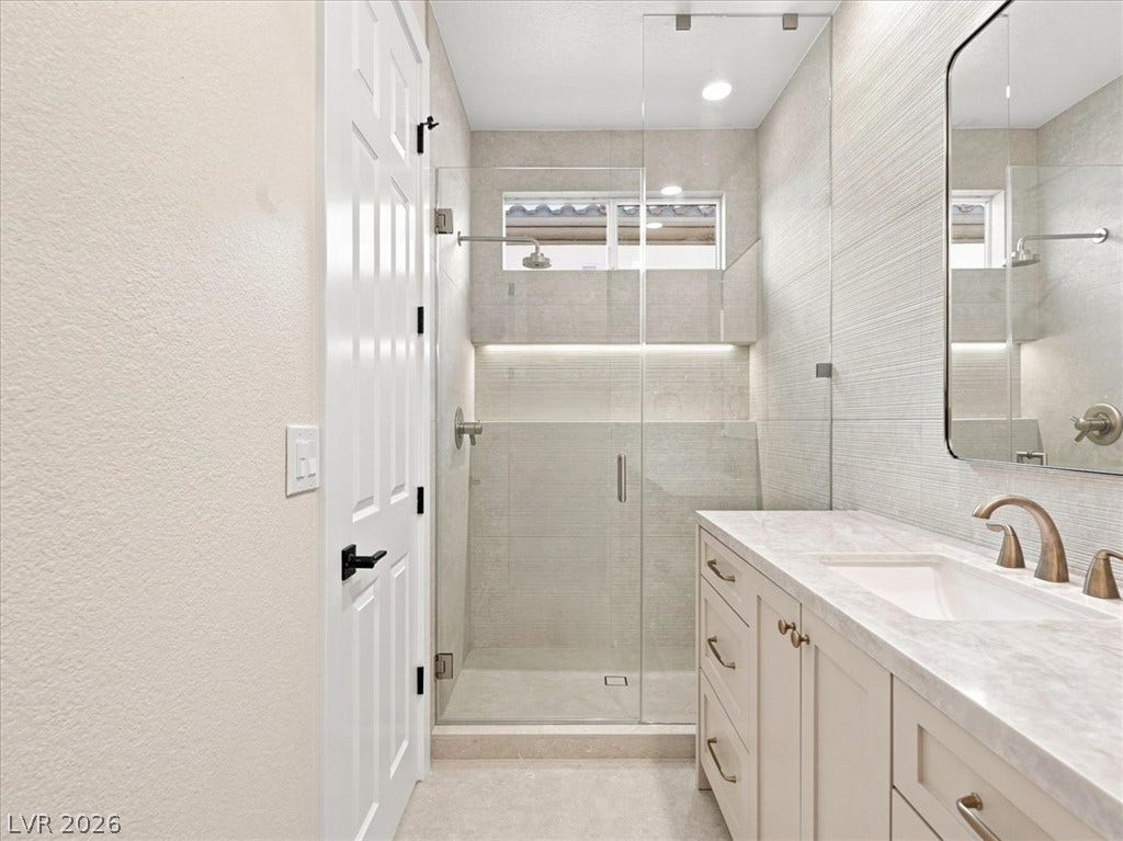 A glass-enclosed walk-in shower complements the single vanity topped with stone counters.