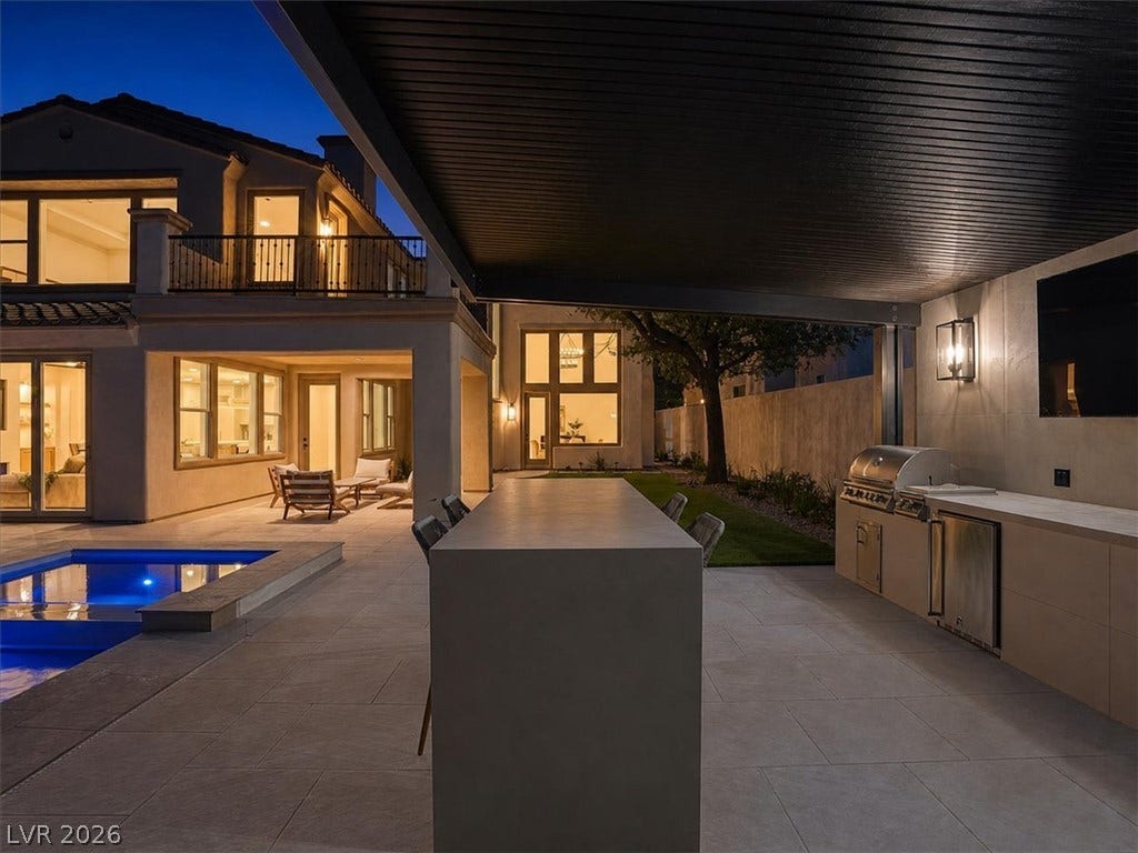 A covered outdoor kitchen features sleek built-in amenities alongside a sparkling swimming pool.