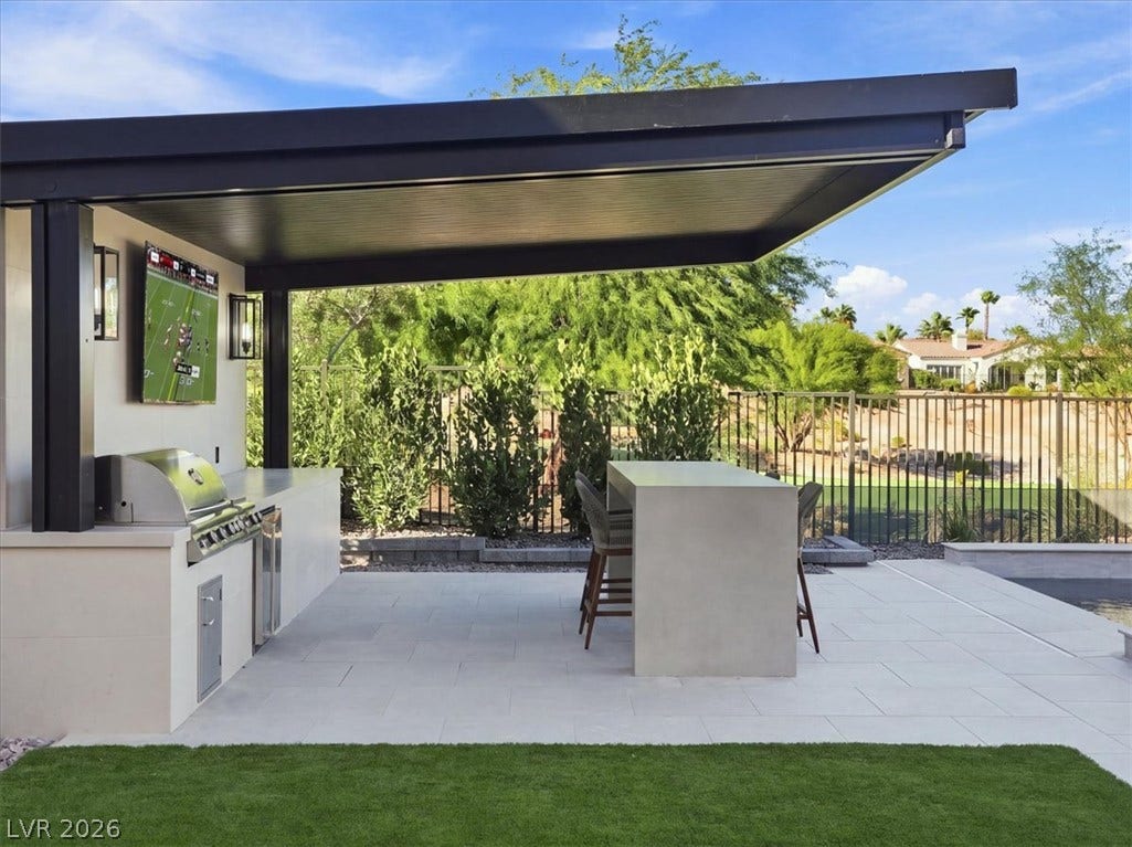 Sheltered outdoor kitchen and bar structure features sleek stone countertops and a modern pavilion roof.