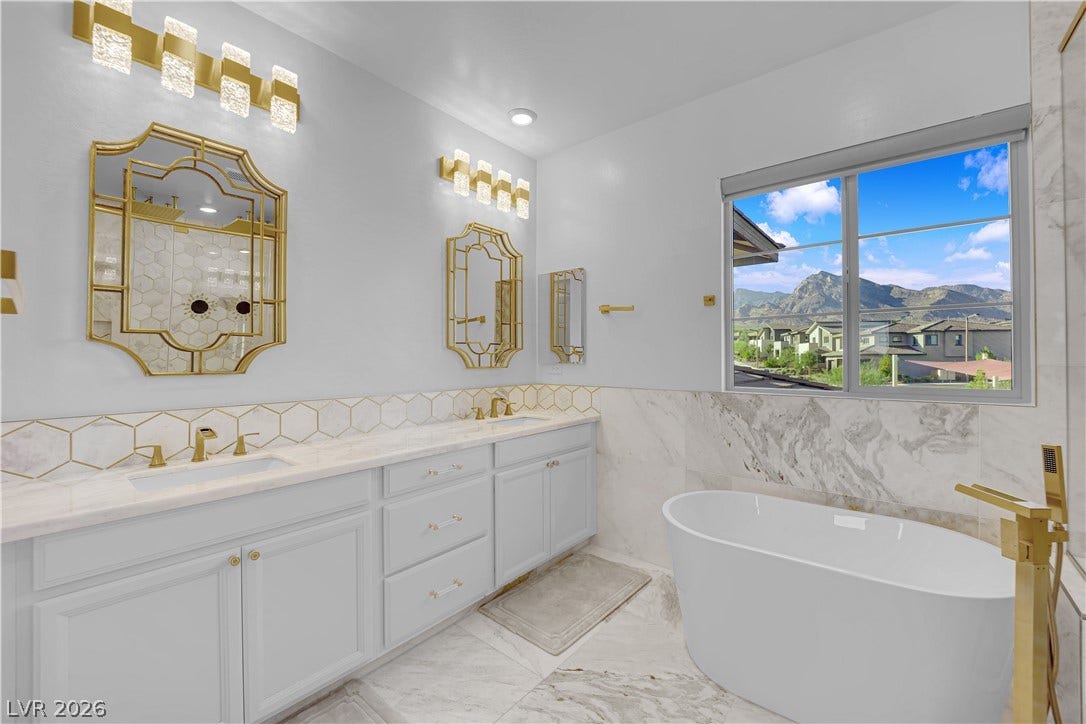 12415 Aster Hills Avenue, Las Vegas, NV 89138 Marble finishes and gold hardware surround a modern soaking tub beneath picturesque mountain views.
