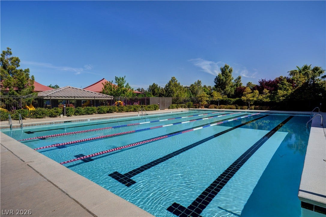 218 Crooked Putter Drive, Las Vegas, NV 89148 An expansive outdoor lap pool sits framed by green trees under a clear blue sky.