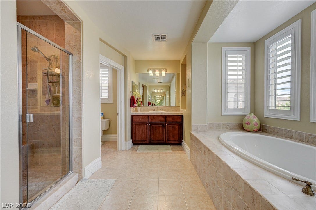 218 Crooked Putter Drive, Las Vegas, NV 89148 A spacious bathroom features tiled flooring, a glass-enclosed shower, and a built-in soaking tub.