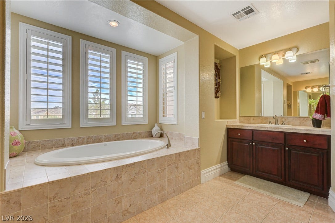 218 Crooked Putter Drive, Las Vegas, NV 89148 A deep soaking tub sits beneath plantation shutters in this spacious primary bathroom.