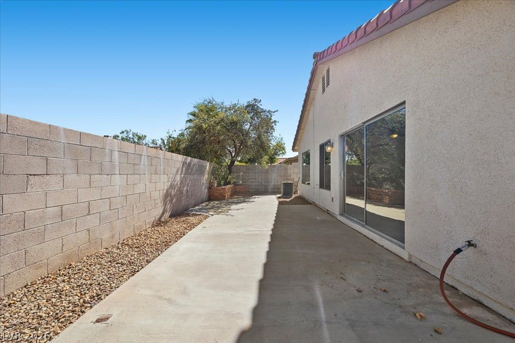 2432 Millcroft Drive, Henderson, NV 89074 A long concrete patio sits alongside the stucco exterior under clear blue skies.
