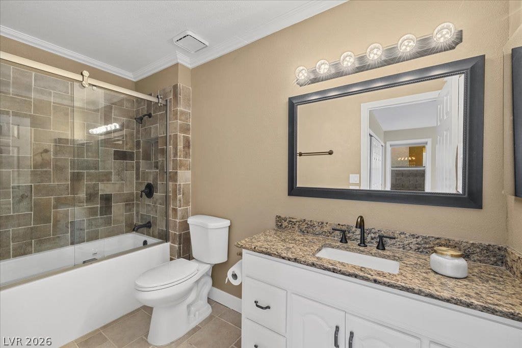 2432 Millcroft Drive, Henderson, NV 89074 Earth-toned tile surrounds a glass-enclosed tub alongside a granite-topped vanity.