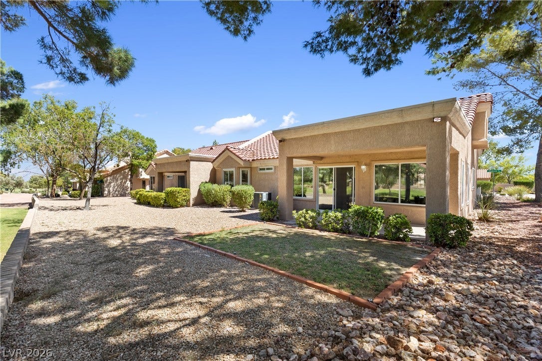 Mature trees shade the low-maintenance desert landscaping surrounding this stucco exterior.