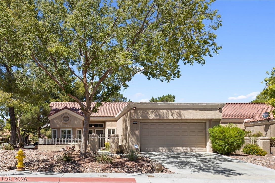 Mature trees frame a charming tile-roofed home with an attached garage.