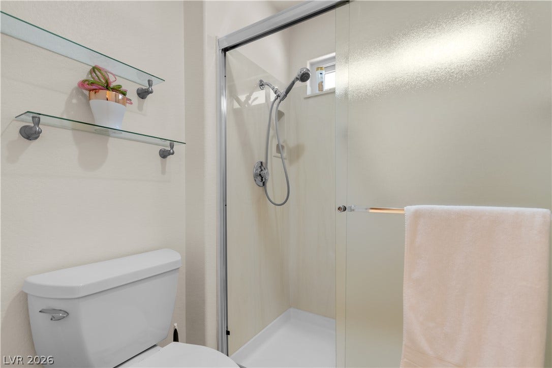 Glass doors enclose a modern walk-in shower situated adjacent to floating display shelves.