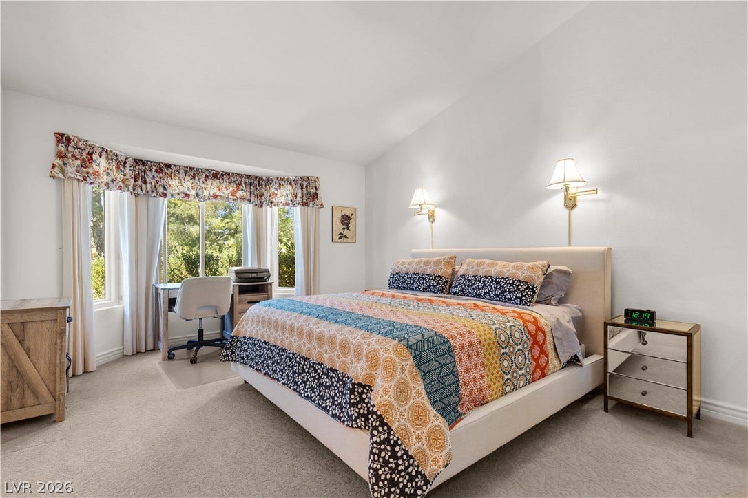 Plentiful natural light streams through a wide bay window in this carpeted bedroom.