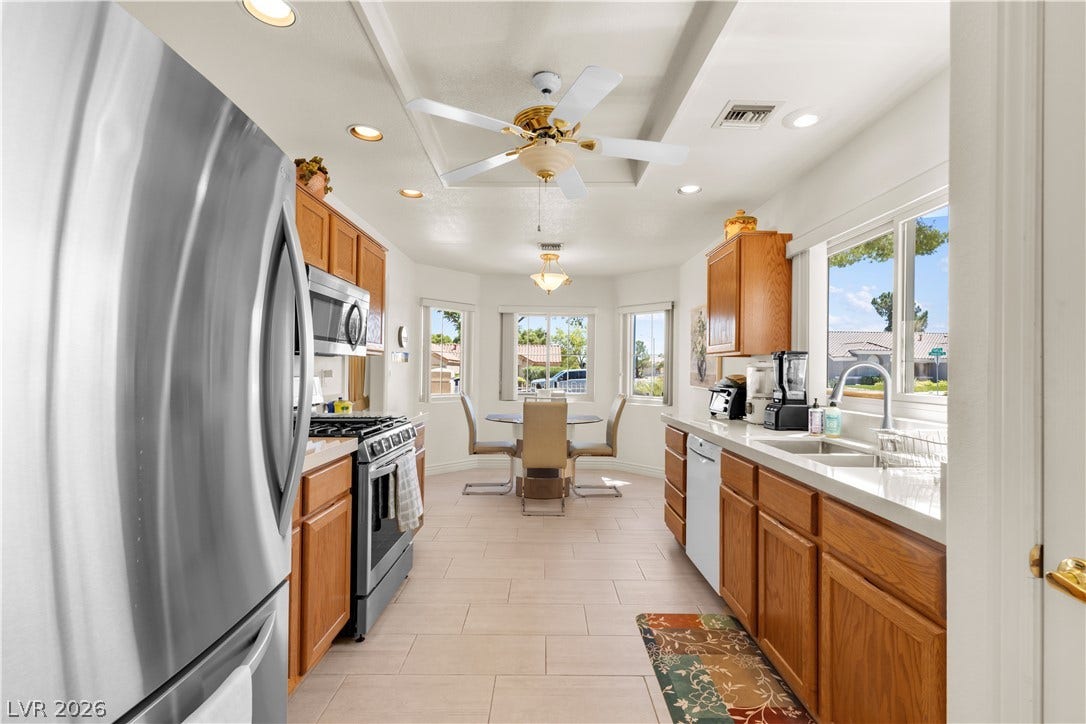Ample wooden cabinetry and tile floors frame this functional galley layout leading to a sunny dining nook.