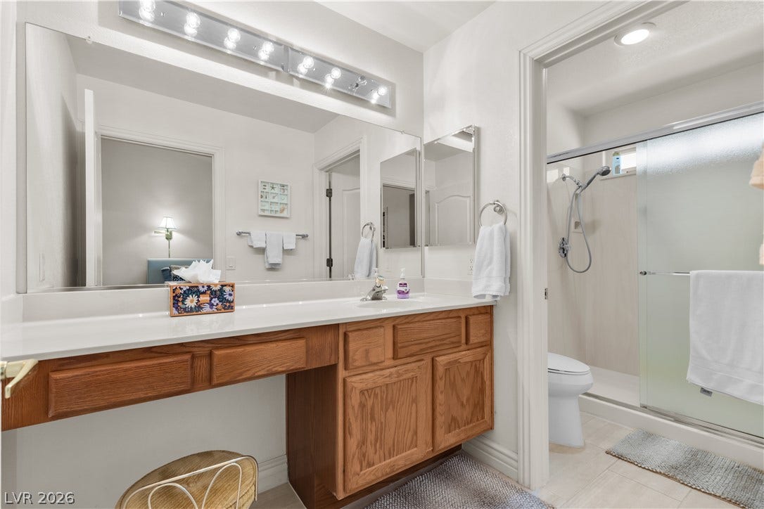 A spacious vanity with natural wood cabinetry stands adjacent to a tiled walk-in shower.