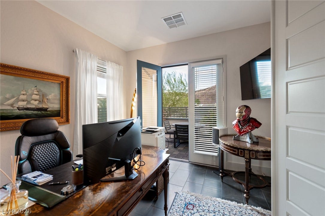 A quiet home office features durable tile flooring and access to a private patio.