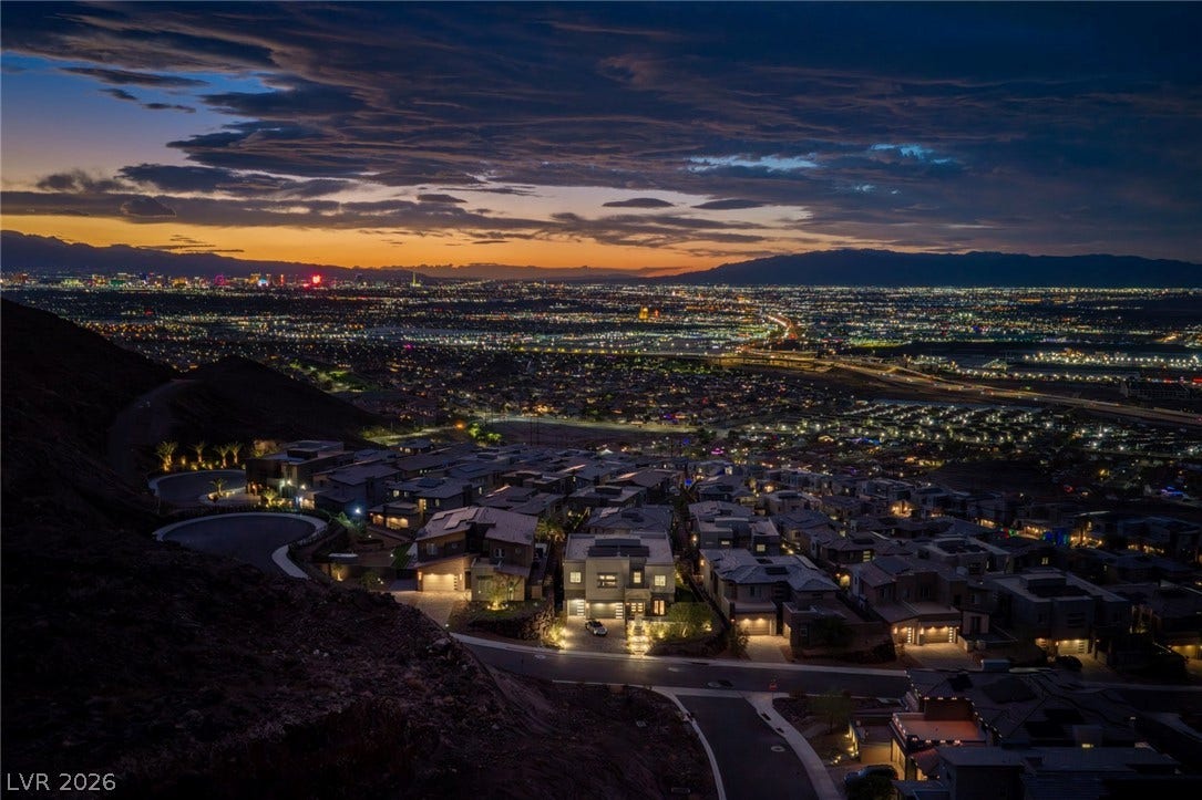 Glimmering city lights spread across the valley floor beneath a dramatic twilight sky.