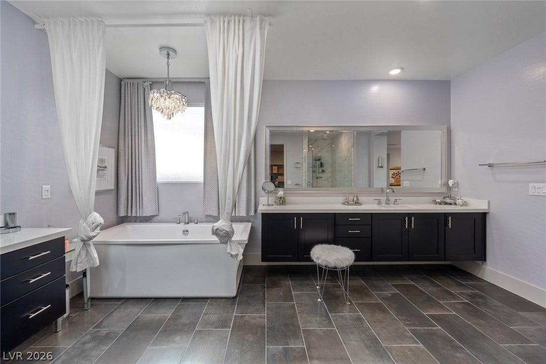 Dark tile flooring runs throughout a spacious primary bath featuring a deep soaking tub.