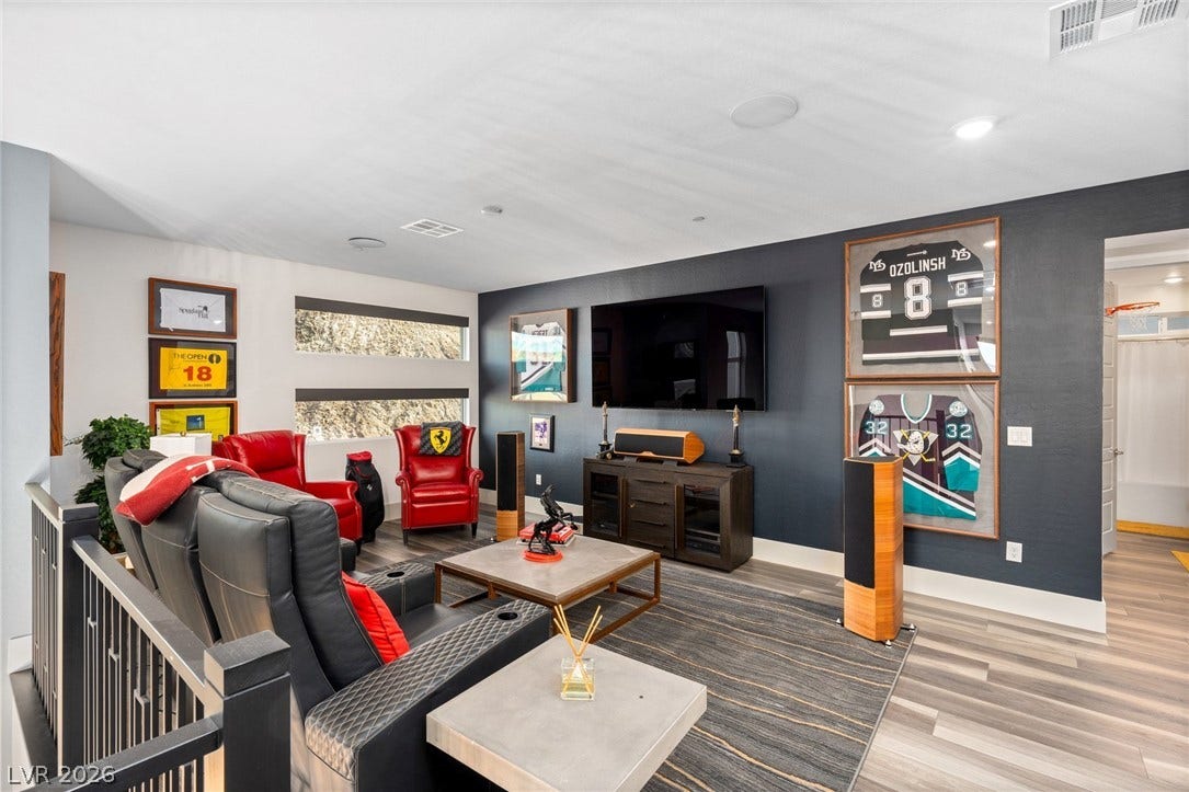 An inviting lower-level media room showcases sleek wood-style flooring and high ceilings with recessed lighting.