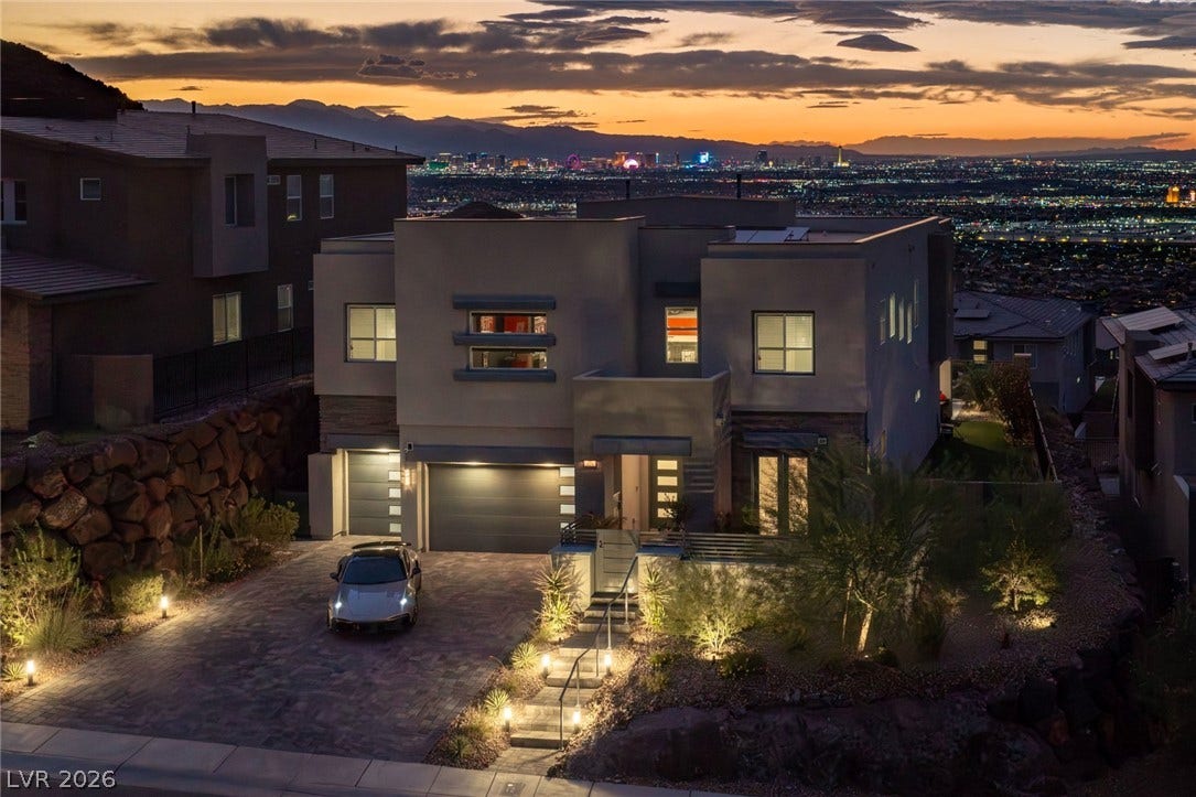 A modern multi-level residence captures twinkling city lights and mountain backdrops at twilight.