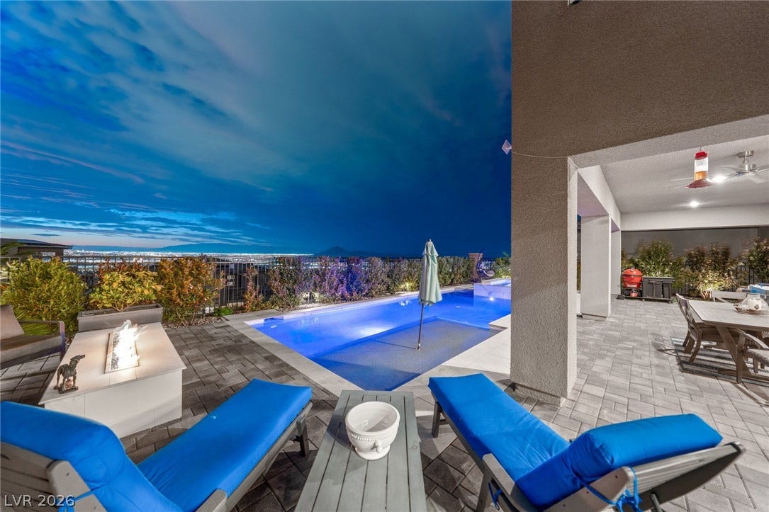 An inviting backyard oasis overlooks city lights and distant mountains under a twilight sky.