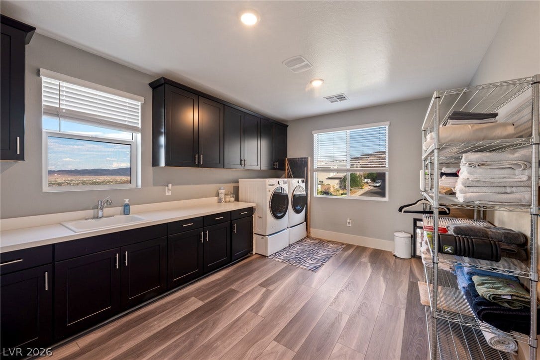 A spacious laundry room features dark cabinetry and wood-look flooring under recessed lighting.