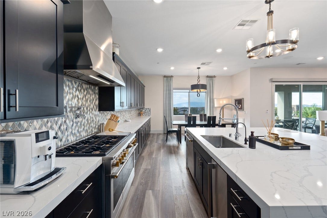 A spacious kitchen features a long marble-patterned island alongside dark wood cabinets.