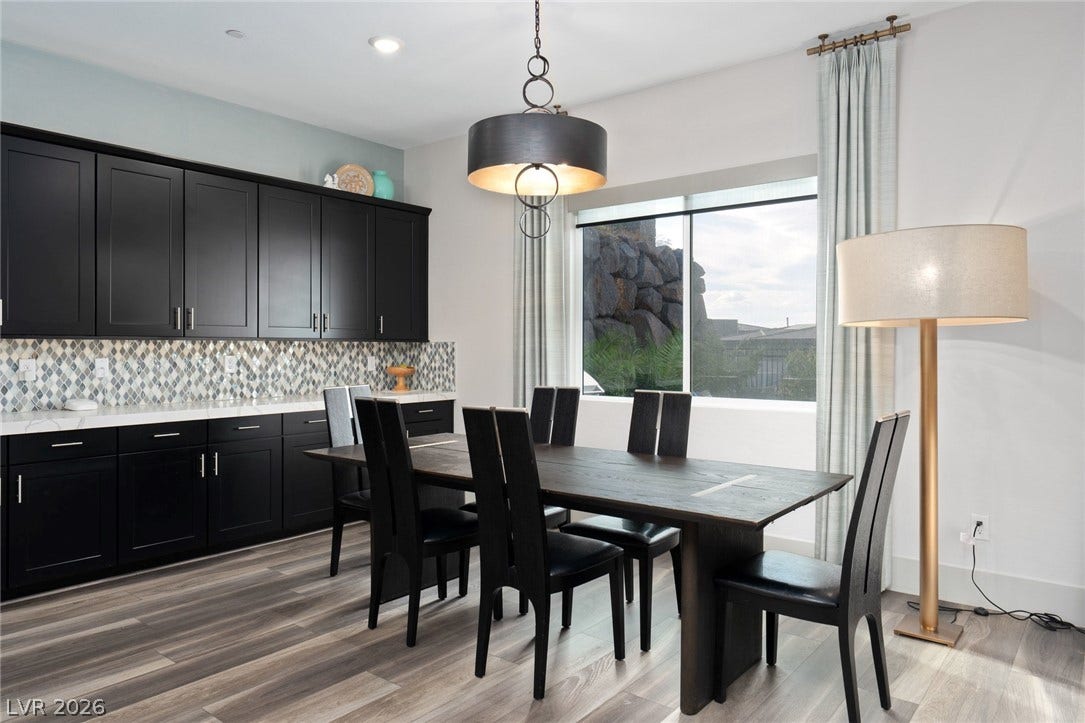 Dark cabinetry and wood-look flooring frame a dining area centered around a wide window.