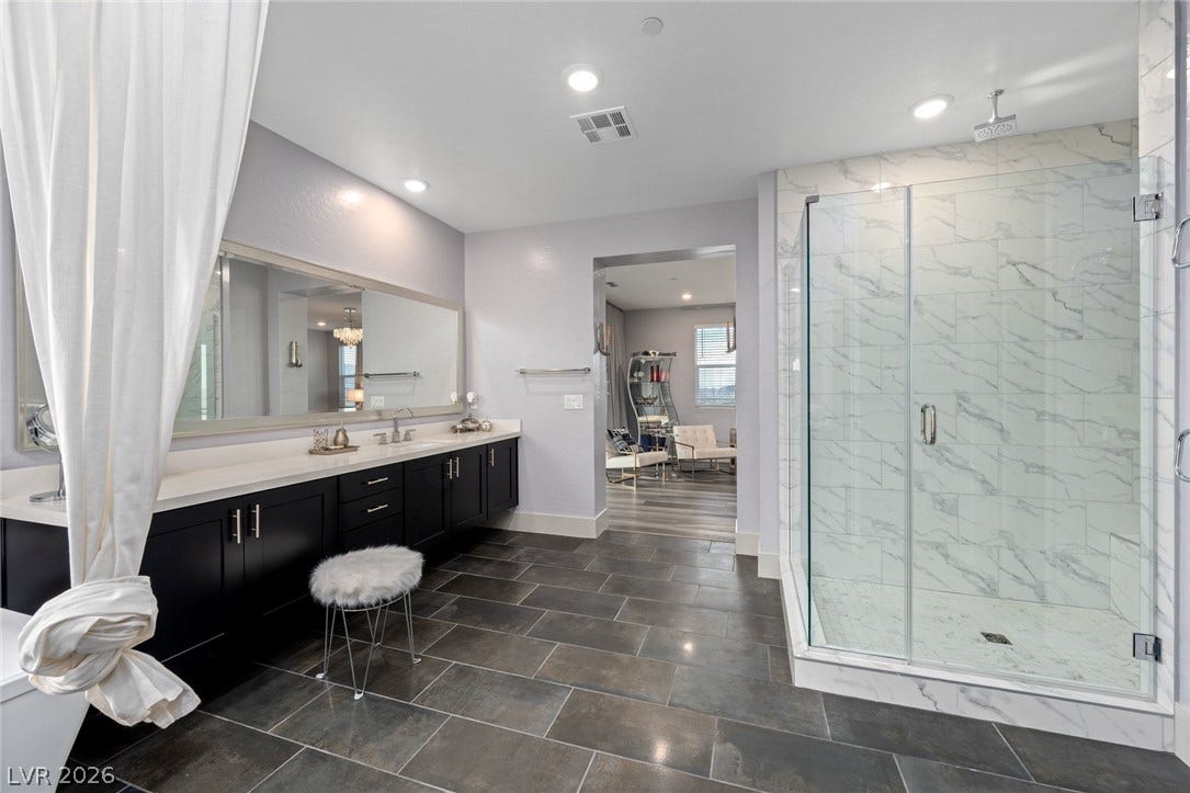 A spacious bathroom features a modern glass-enclosed walk-in shower and large stone-patterned floor tiles.