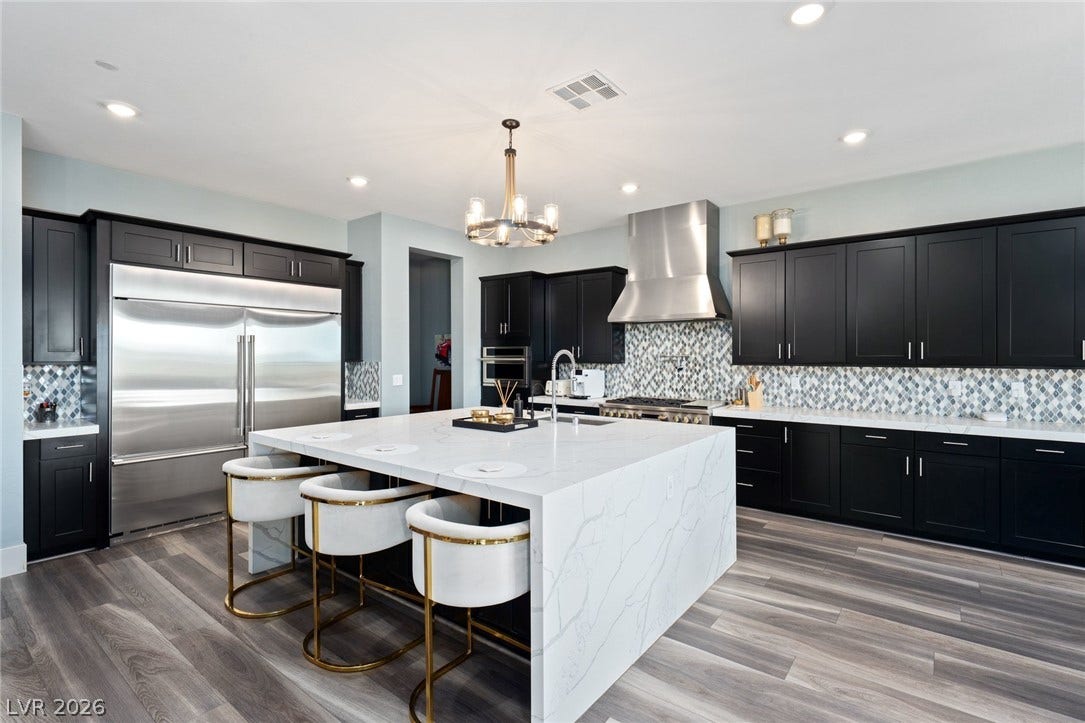Streamlined dark cabinetry contrasts beautifully with a massive stone waterfall island and patterned backsplash tile.