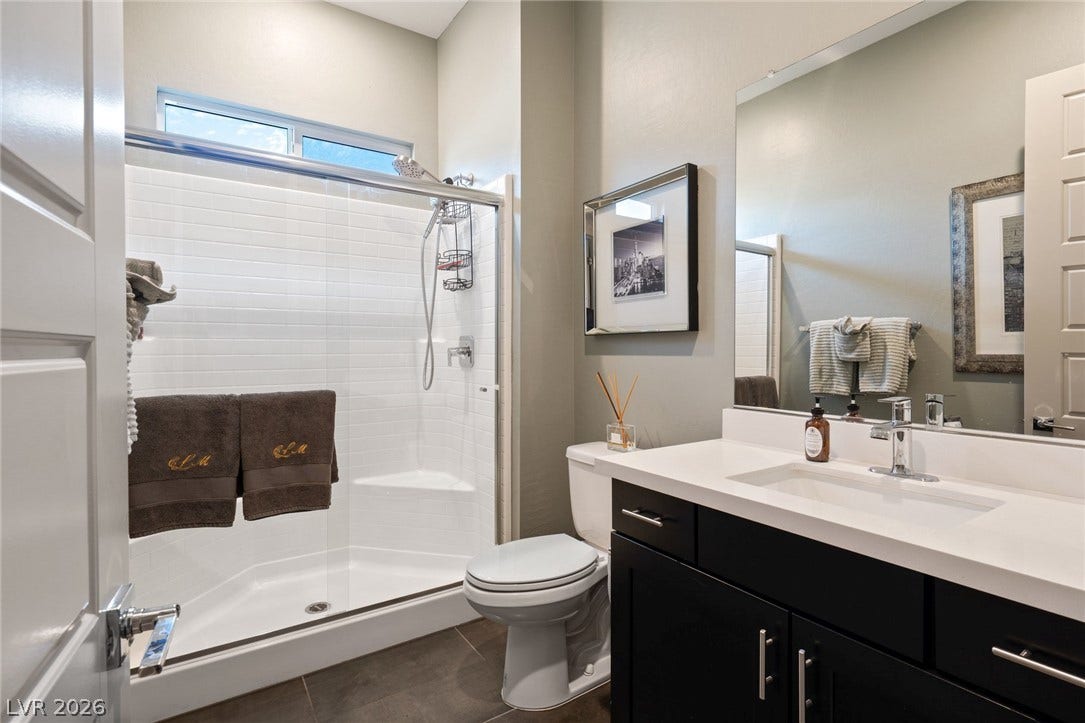 A glass-enclosed shower with white subway tile highlights this functional bathroom with dark cabinetry.