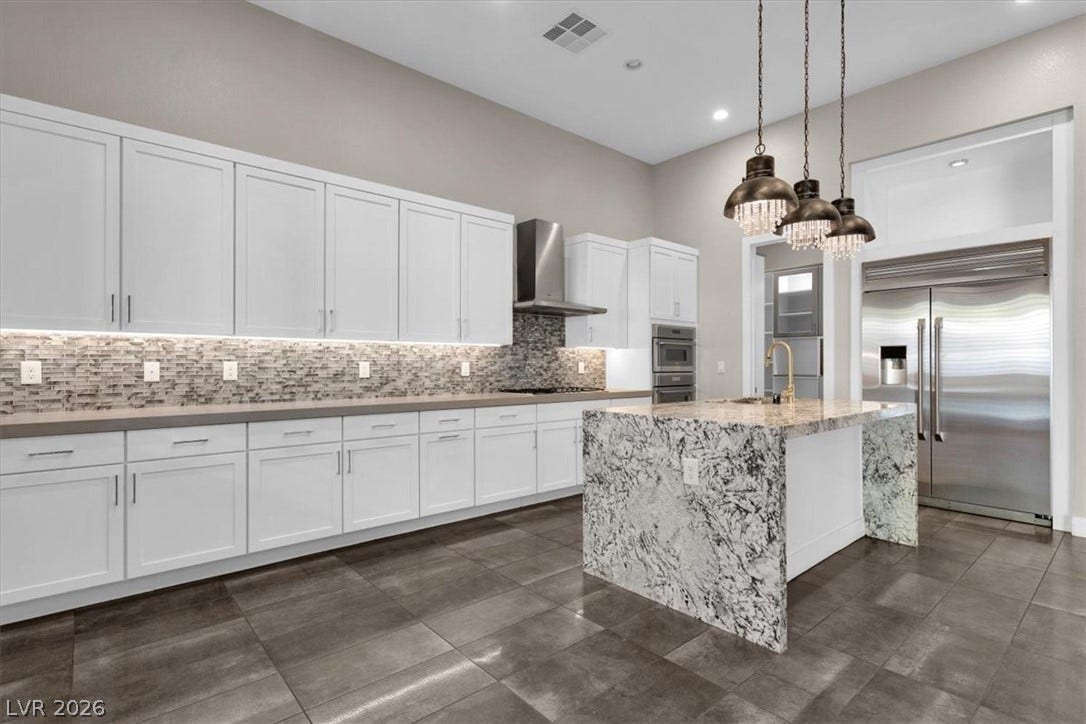Kitchen with stainless steel appliances, tasteful backsplash, white cabinets, light stone countertops, and an island with sink, and breakfast nook