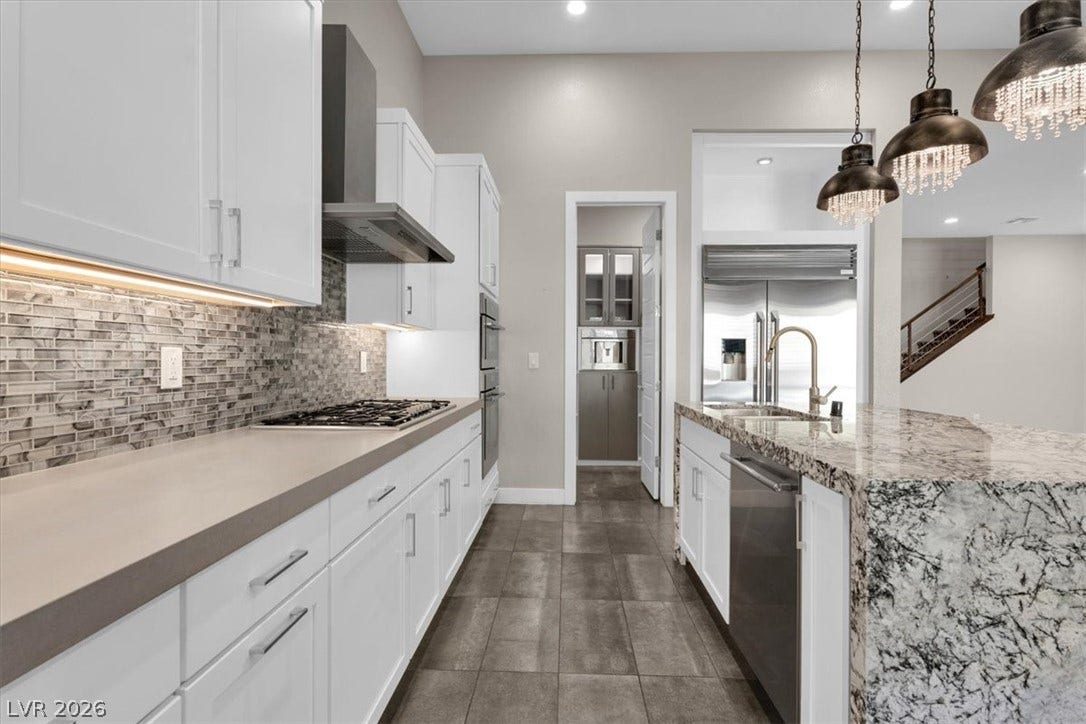 Kitchen featuring white cabinets, a center island with sink, light stone counters, and stainless steel appliances and walk in pantry wtih Thermador coffee maker