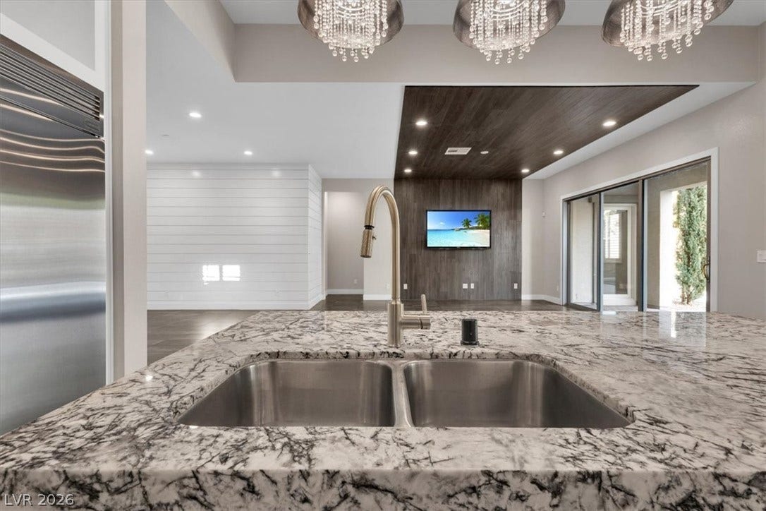 Kitchen featuring built in Monogram refrigerator, light stone counters, open floor plan, and hanging lights, with views to the open plan living area and pool