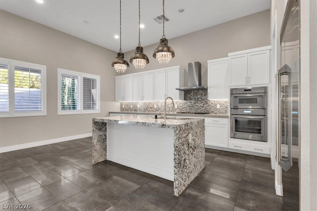 Kitchen with light stone counters, Thermador stainless steel appliances, tasteful backsplash, white cabinetry, and a center island
