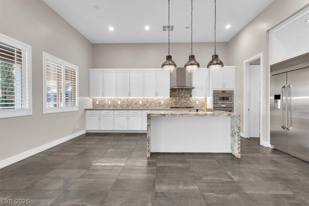 Kitchen featuring white cabinets, Thermador and Mongram stainless steel appliances, backsplash, light stone counters, and a large kitchen island