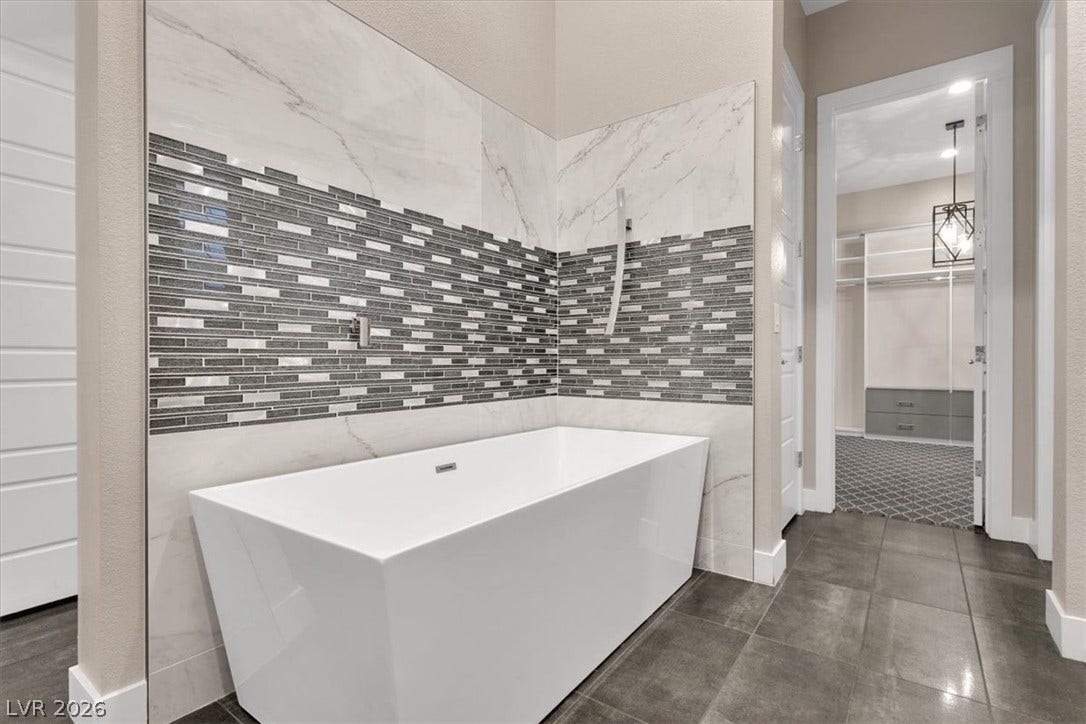 Bathroom featuring a freestanding tub, a spacious walk in closet, and tile walls