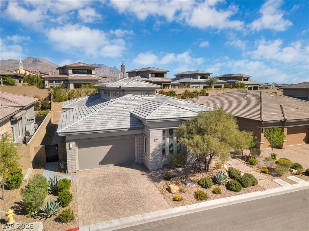 View of front of home featuring an attached garage, decorative driveway, stucco and brick siding, and lush landscaping